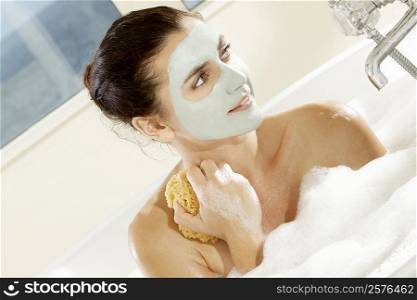 Close-up of a young woman with a facial mask holding a bath sponge