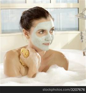 Close-up of a young woman with a facial mask holding a bath sponge