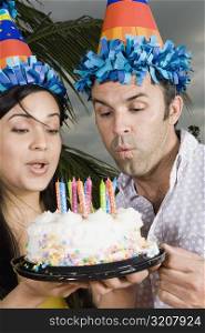 Close-up of a young woman with a mid adult man blowing candles on a birthday cake
