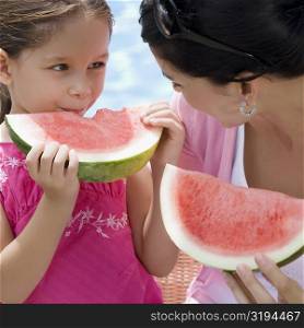 Close-up of a young woman with her daughter eating watermelon slices