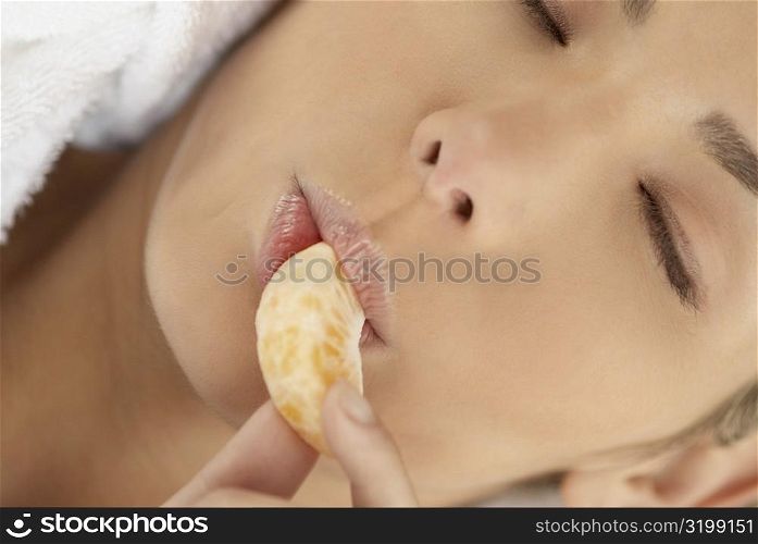 Close-up of a young woman with her eyes closed and eating an orange