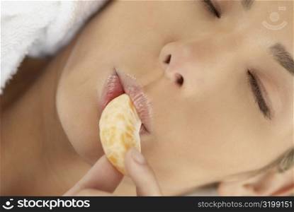 Close-up of a young woman with her eyes closed and eating an orange