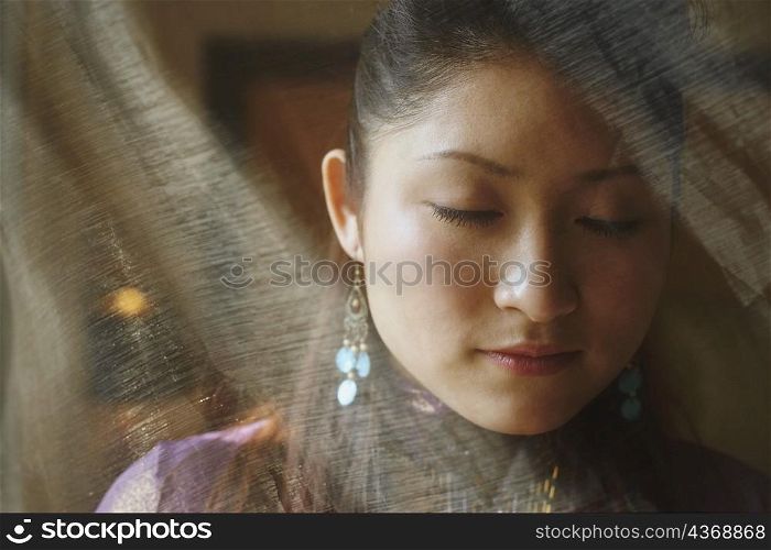 Close-up of a young woman with her eyes closed hiding behind a transparent curtain