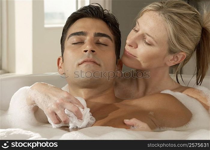 Close-up of a young woman with her eyes closed scrubbing a young man&acute;s chest with a bath sponge