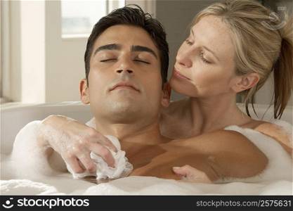 Close-up of a young woman with her eyes closed scrubbing a young man&acute;s chest with a bath sponge