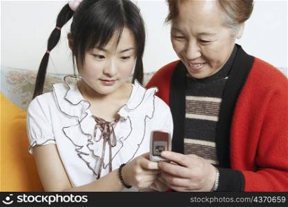 Close-up of a young woman with her grandmother holding a mobile phone