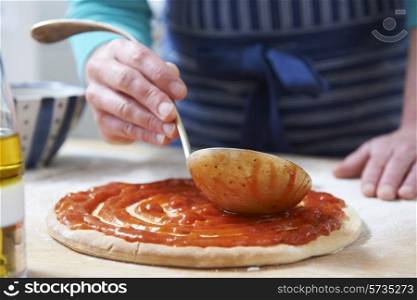Close Up Of Adding Tomato Sauce To Pizza Base