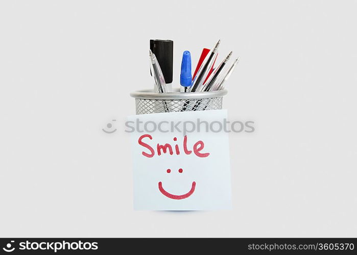 Close-up of adhesive notepaper with smiley face stuck on pen holder over white background
