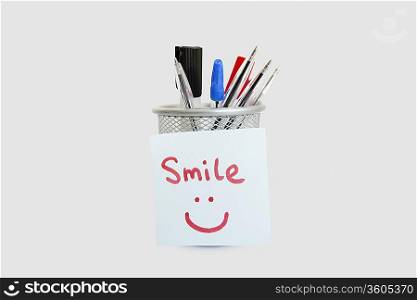 Close-up of adhesive notepaper with smiley face stuck on pen holder over white background