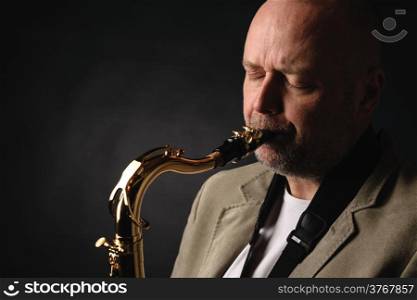 Close up of adult musician playing tenor saxophone eyes closed, dark background