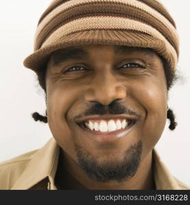 Close up of African-American mid-adult man wearing knit hat with brim smiling at viewer.