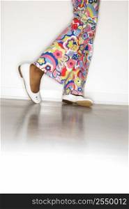 Close-up of African-American teen girl&acute;s legs with floral pants and white shoes against white background.