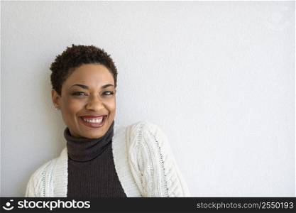 Close up of African- American woman standing against white wall looking at viewer and smiling.