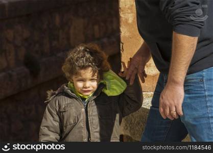 Close-up of an adorable little boy with curly hair about to grab his father&rsquo;s hand on an out of focus background. Family concept.. Little boy about to grab his father&rsquo;s hand