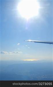 Close up of an aeroplane wing in the sky with the sun shining bright above