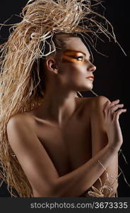 close up of an amazing woman in ethnic style with creative make up and raffia on the head doing hairstylish. She is in front of the camera, her face is turned on profile and her right hand is near the left shoulder