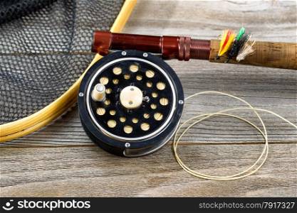 Close up of an antique fly fishing reel, rod, landing net and artificial flies on rustic wood. Layout in horizontal format.