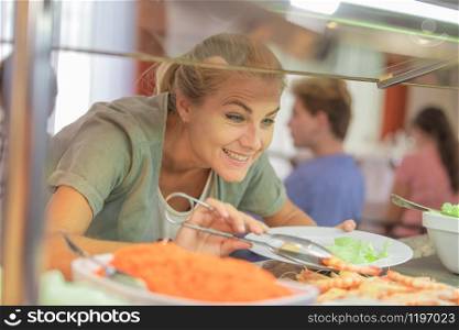 Close-up of an attractive adult woman serving herself food with stainless steel serving tongs at a cafeteria. eating concept.. Woman serving herself at a cafeteria
