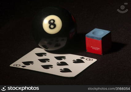 Close-up of an eight ball with cue chalk and a playing card on a pool table