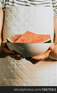 Close up of an old waitress offers and holds a watermelon in a bowl, fruits, healthy life, good eating, mediterranean concepts, copy space, vertical image