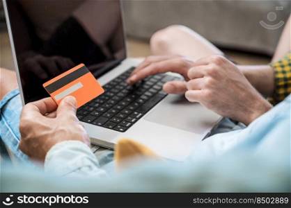 Close up of an unrecognizable gay couple using laptop computer while sitting on a couch at home, shopping online with a credit card. High quality photography.. Close up of an unrecognizable gay couple using laptop computer while sitting on a couch at home, shopping online with a credit card