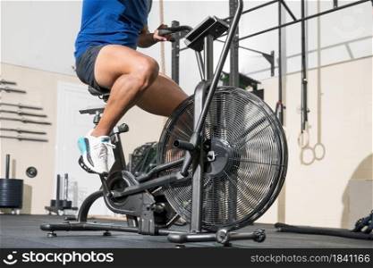 Close up of an unrecognizable man doing cardio training on stationary air bike machine with fan at the gym. High quality photo. Close up of an unrecognizable man doing cardio training on stationary air bike machine with fan at the gym.