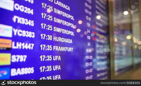 Close-up of arrival and departure board in airport. Flight information on blue field with language changing from English to Russian.