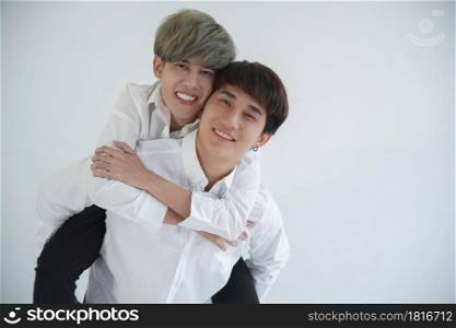 Close up of Asian attractive LGBT young gay couple riding on back and hugging in the room on white background
