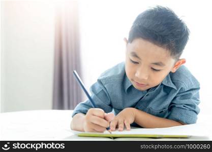 Close up of asian boy using a pencil writing ,drawing on a white book on bedroom.Happy asian kid is using a pencil to do his homework.
