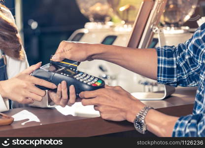 Close-up of asian customer using his credit card to swipe with EDC to pay a barista for his coffee purchase at a cafe bar.