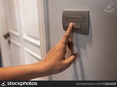 Close up of Asian female right hand is turning on or off on grey light switch over textile texture wall in Luxury house. Copy space.