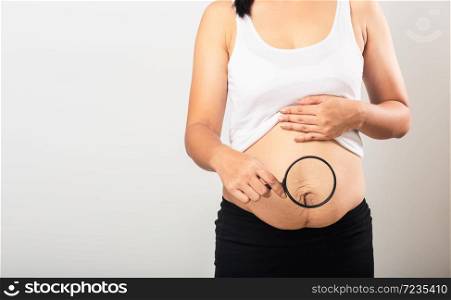 Close up of Asian mother woman use magnifying glass show stretch mark loose lower abdomen skin she fat after pregnancy baby birth isolated on white background, Healthy belly excess body concept
