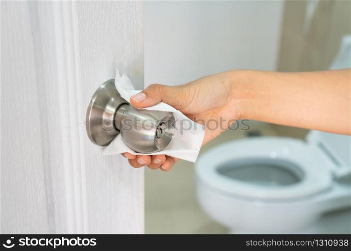 Close up of Asian woman hand using white toilet paper touch the public toilet door knob to prevent direct contact and prevent infection, virus, bacteria germs and dirt.