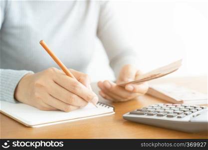 Close-up of asian woman using calculator counting and make note calculate about cost at home.