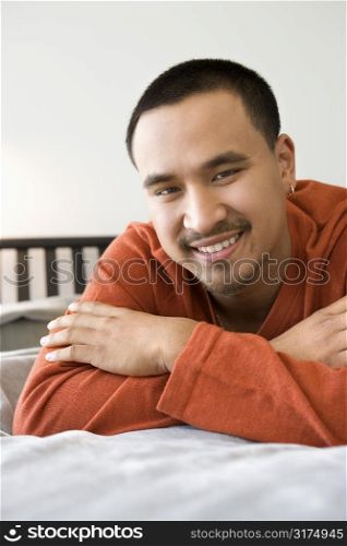Close-up of Asian young adult man lying on bed looking at viewer smiling.