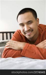 Close-up of Asian young adult man lying on bed looking at viewer smiling.