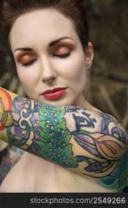 Close-up of attractive Caucasian nude woman&acute;s face and tattooed arm.