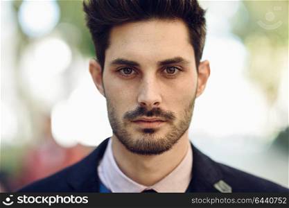 Close-up of attractive man in the street in formalwear. Young bearded businessman with modern hairstyle in urban background.