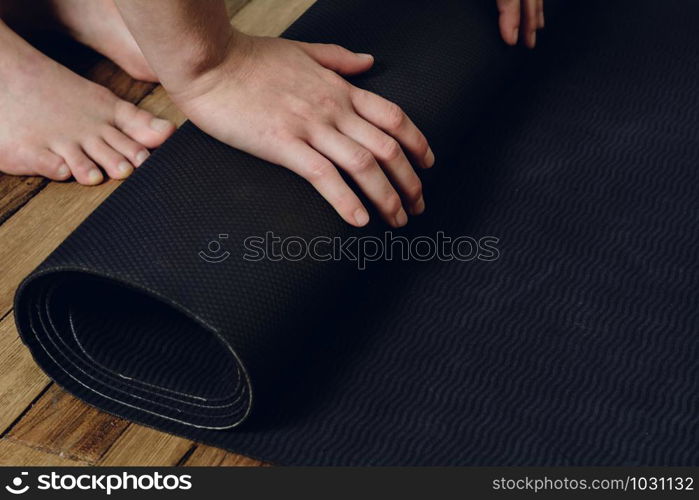 Close-up of attractive young woman rolling her fitness mat before or after yoga class at home. Healthy life concept.