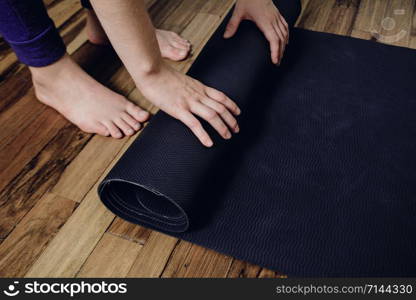 Close-up of attractive young woman rolling her fitness mat before or after yoga class at home. Healthy life concept.