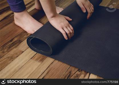 Close-up of attractive young woman rolling her fitness mat before or after yoga class at home. Healthy life concept.
