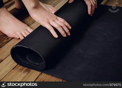 Close-up of attractive young woman rolling her fitness mat before or after yoga class at home. Healthy life concept.