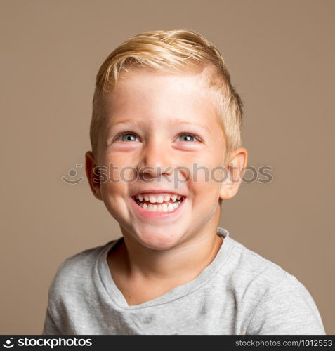 Close up of Baby boy smiling three year old, blond with green eyes on a light brown background, conceptual photo for dental hygiene and personal care.