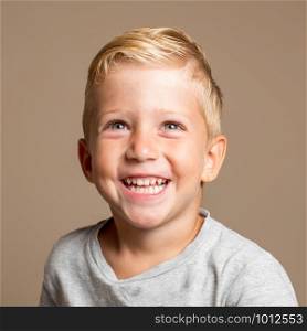 Close up of Baby boy smiling three year old, blond with green eyes on a light brown background, conceptual photo for dental hygiene and personal care.