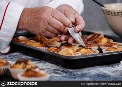close-up of baker&rsquo;s hands putting chocolate on muffins
