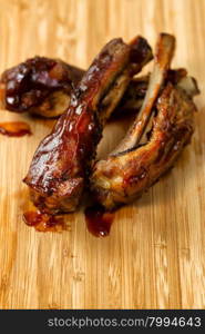 Close up of barbecued ribs with sauce on wooden cutting board. Selective focus on upper front part of ribs in vertical format.