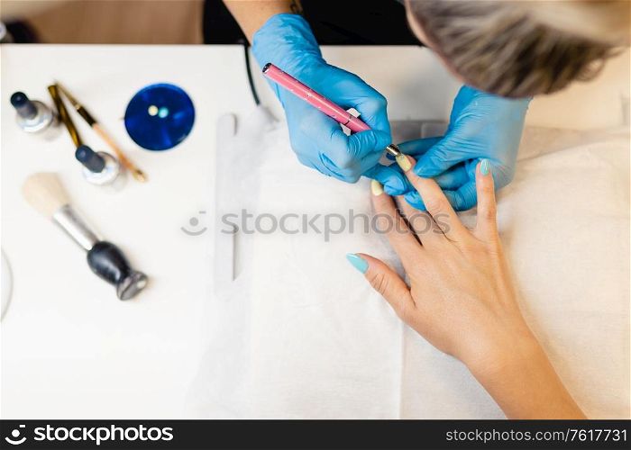 Close-up of Beautician painting her client&rsquo;s nails in blue and yellow nail varnish in a beauty centre. Close-up of Beautician painting her client&rsquo;s nails in blue and yellow nail varnish.