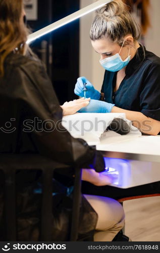 Close-up of Beautician painting her client&rsquo;s nails in blue and yellow nail varnish in a beauty centre. Close-up of Beautician painting her client&rsquo;s nails in blue and yellow nail varnish.