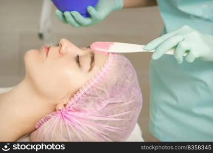 Close up of beautician’s hand applying alginate mask on the face of the young caucasian woman in a beauty salon. Hand applying alginate mask on face