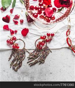 Close up of beautiful earrings with currants, rose petals and ch&agne glass at grey concrete table. Celebrating valentines day with jewelry gift and romantic drink. Top view.